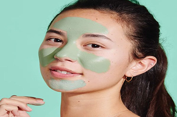 Close up of an Asian female model wearing Kinship's green mint clay mask in a studio setting, on a green mint background.
