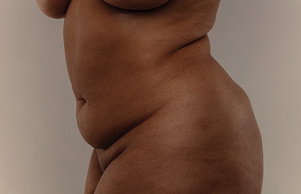 A close up studio image of a woman's body showing her skin, tummy, thighs, bottom and belly button against a grey background