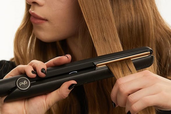 model straightening her hair using a black ghd original styler on her copper coloured hair