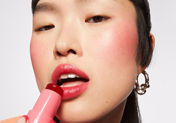 An Asian model in a studio setting looks at the camera as she applies the Milk Makeup Cooling Water Jelly Tint to her lips