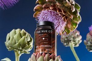 a jar of nue co supplements surrounded by exotic flowers against a blue background