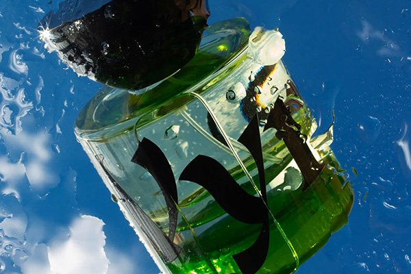 a bottle of green vyrao i am verdant perfume shot in water with a blue sky behind it.