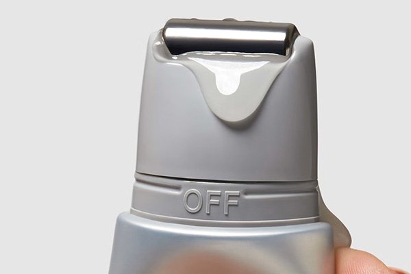 An extreme close up of the top part of a product with a model’s hands squeezing while a lightweight liquid is dripping down.