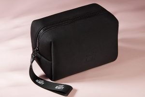 a black neoprene bag from cult beauty shot against a pink background shot in a studio.