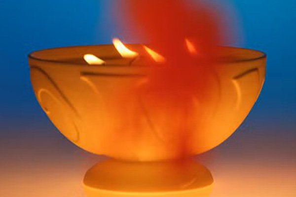 A close up of a still life image of a multi-wick Vyrao candle burning with a haze of orange smoke against a dusky blue background