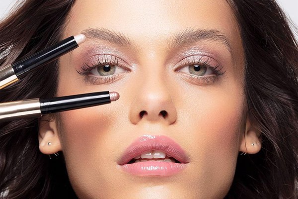 A close up of a female model with bridal make up wearing By Terry beauty and holding two kohl eyeshadows to her face.