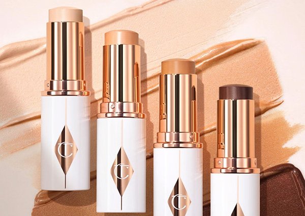 A studio image showing a range of shades of the new Charlotte Tilbury Unreal Skin Sheer Glow Tint with packaging and swatches