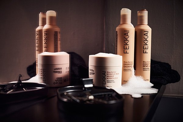 A wide product shot of Fekkai’s She Butter shampoo, conditioner and hair mask sat on a bathroom shelf in a bathroom setting.