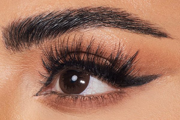 huda false eyelashes applied to a models dark brown eyes. she is looking away from the camera. her eyebrows are dark brown and arched