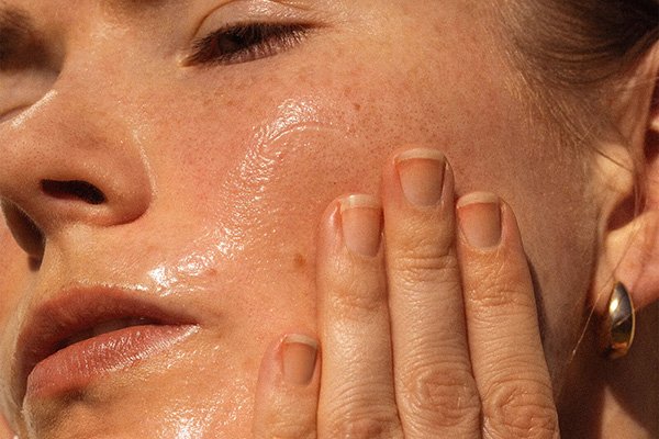 A close up image of a female model massaging Alpha-H’s Melting Moment Cleansing Balm into her case while looking up to the sunlight.