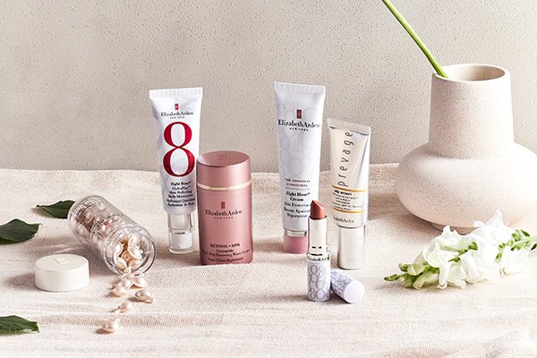 A wide shot image of Elizabeth Arden’s betsellers standing on a table with green leaves and a ceramic vase in a studio setting.