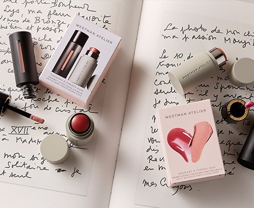 Westman Atelier beauty products, including the Squeaky and Cheeky Duo, sit on an open book with French writing across the page.