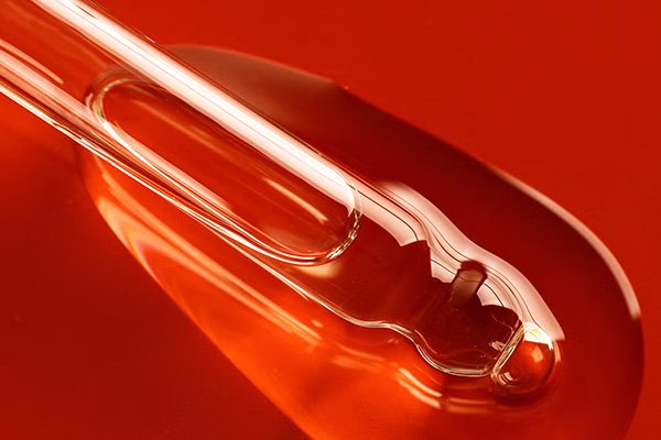 An extreme close up shot of a pipette filled with a clear oil that is spilling onto a dark red background in a studio setting.