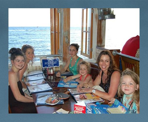 Maddie Edwards on holiday with her family, sitting around a table with her sisters and her mum, all smiling with the sea in the background