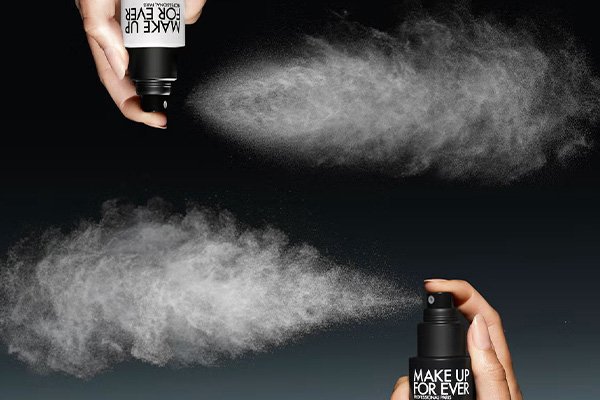 two different makeup forever setting sprays being spritzed against a black ground in a studio