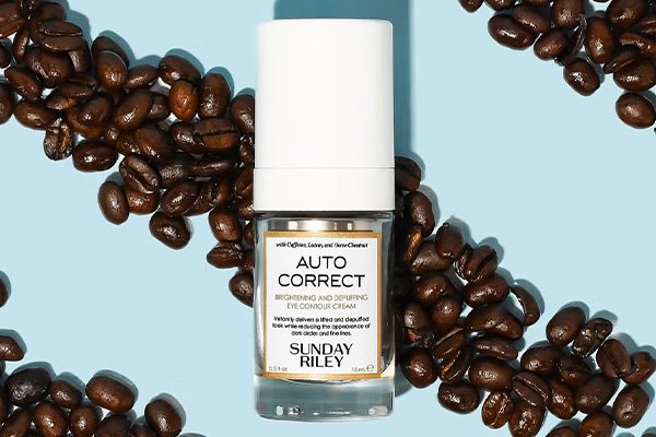 a close up of sunday rileys eye cream shot on a blue background with coffee beans surrounding the bottle