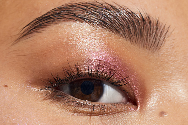 close up of a brown eye. Pink eye shadow is on the lid and the brown eyebrows are brushed up and defined