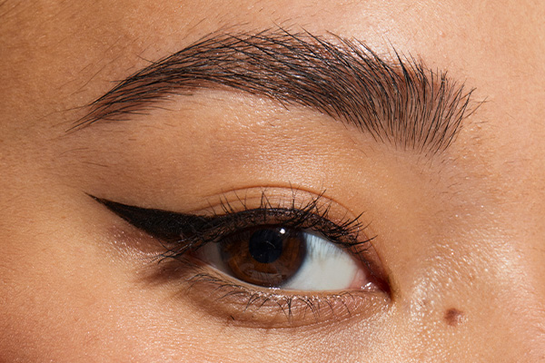 close up of a models eye. she has a cat eye using black eyeliner and her eyes are brown. image is a close up of only one eye