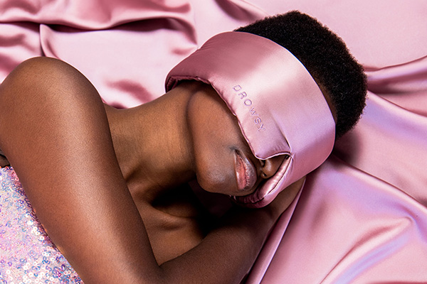 An image of a female model asleep on her Drowsy pink silk pillowcase and wearing her Drowsy pink silk eye mask. 