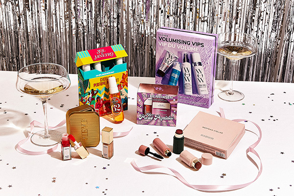 A wide shot image of beauty secret santa gifts laid out on a festive decorated table with glasses of prosecco and metallic confetti. 