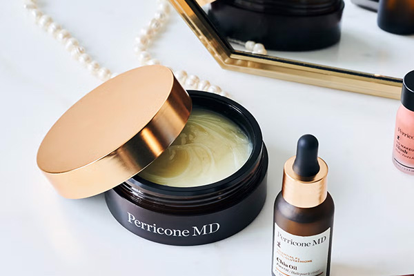 A lifestyle shot of Perricone MD Essential Fx Acyl-Glutathione range on a white marble vanity table with pearls and a gold mirror.