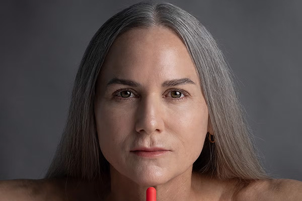 A close up of a female, mature model with grey, long hair looking straight into the camera after putting on her retinol serum. 