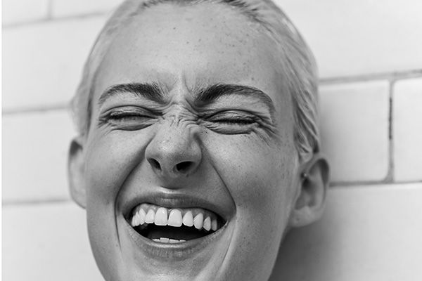 A black and white close up of a female model laughing into the camera with her eyes close, in a studio setting. 