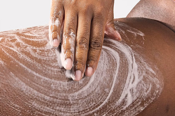 a dark skinned model applying a white exfoliator to her inner thigh. that is all that is seen in the image. shot in a studio