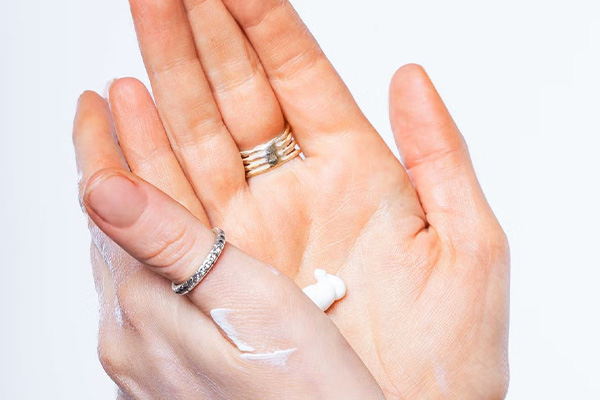 two hands rubbing handcream on them. the models hands have two rings on them- one on the thumb and the other middle finger. shot in a studio