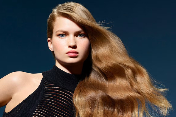 model with long blowdried hair in a light brown hue. her hair is flowing and the image is shot against a dark blue background