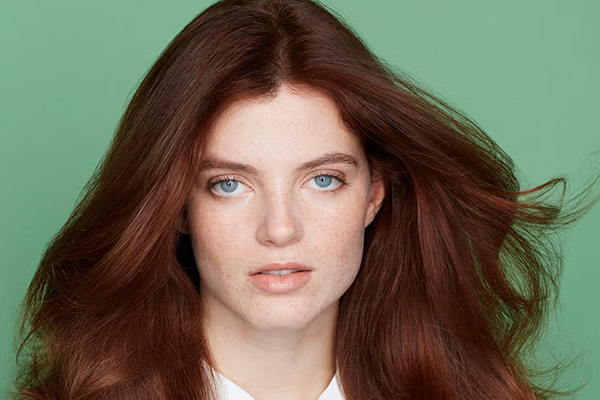 model with red hair, voluminous blow out posing at the camera. image is shot against a green background in a studio