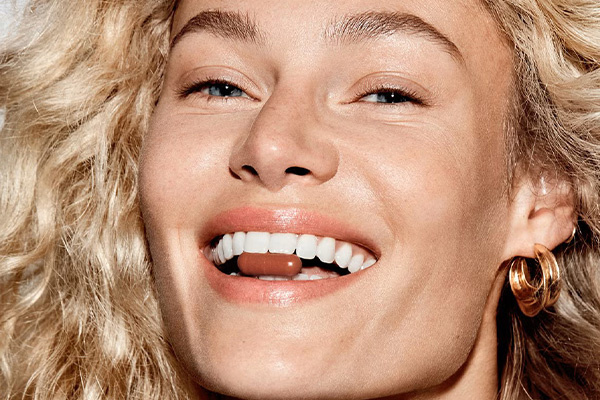 model smiling with a supplement in between her teeth. her hair is curly and blonde