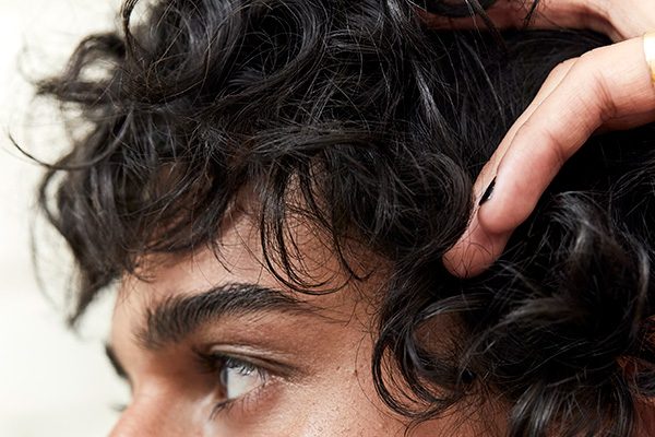 A extreme close up of a male model with dark brown curly hair looking away from the camera, in a studio setting, in front of a white background.