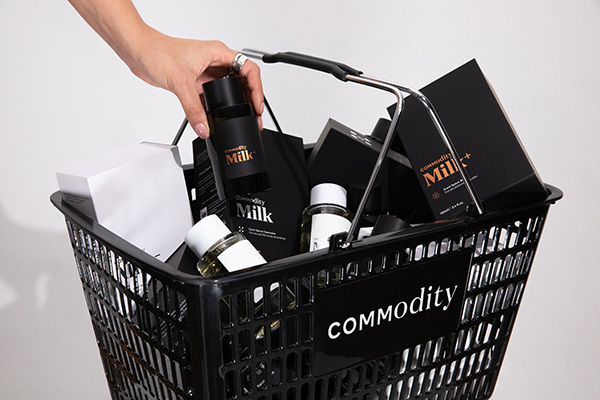 An image of various Commodity fragrances in a Commodity black basket with a hand picking up the milk perfume. In a studio setting, in front of a white background.