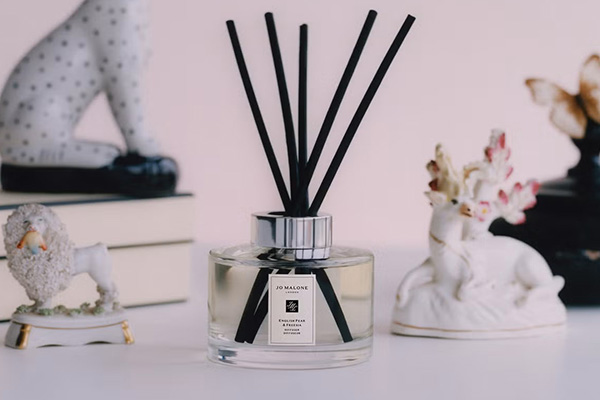 a jo malone reed diffuser sat on a desk surrounded by books and little figurines of opulent animals