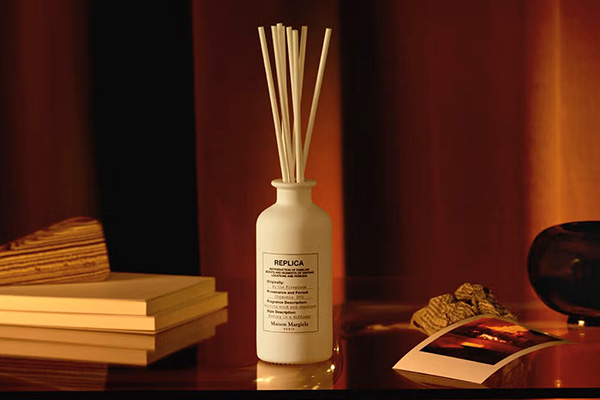 a replica by the fireplace reed diffuser sat on a dark table surrounded by books and a polaroid of a fireplace