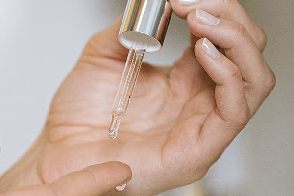 close up image of a womans hands using a pipette of serum dripping it onto her finger tip