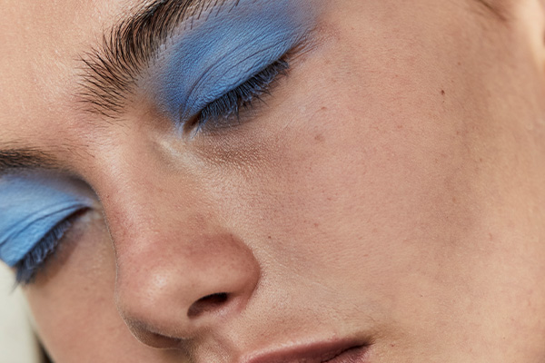 pale skinned model with fluffy eyebrows. close up of her face, eyes are closed and she has blue eyeshadow all over her lids