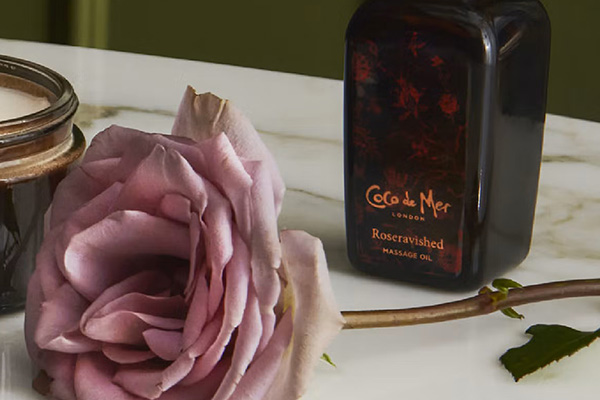 image of a pink rose next to a bottle of coco de mer's massage oil and a candle