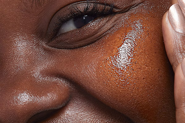 A close up of a female model applying a bakuchiol serum on to her cheek while looking into the camera – in a studio setting.