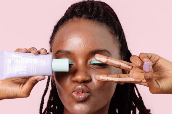 A image of a female model with blue eyeshadow holding Naked Sunday's bestsellers while pouting and putting up the peace signs by her eyes.