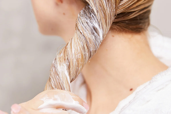 A close up of a female model with blonde hair deep conditioning her hair in the shower setting.