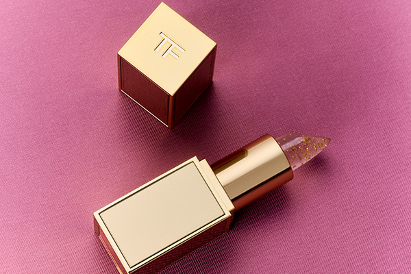A image of TOM FORD Beauty's lip balm lipstick in gold packaging laying on a pink background.