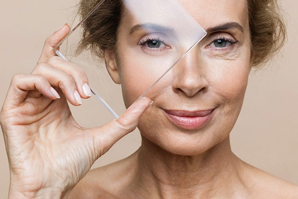 older model holding up a glass to skin showing wrinkle free face
