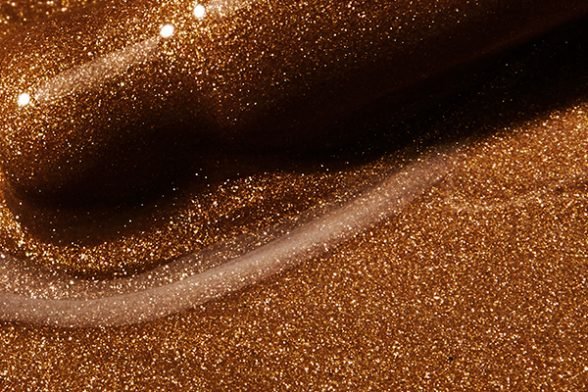 An extreme close up of a medium-to-dark toned bronzing oil formula that features shiny speckles reflective off the liquid.