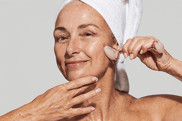 older model with a towel on her head she is using a face roller on her face