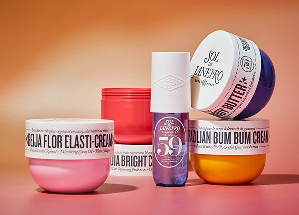 A selection of Sol de Janeiro bestselling products, including the Brazilian Bum Bum Cream, in a studio setting against a pink and orange background.