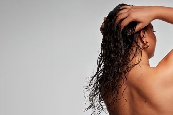 model shot in a studio with wet hair facing the back massaging her wet curly hair