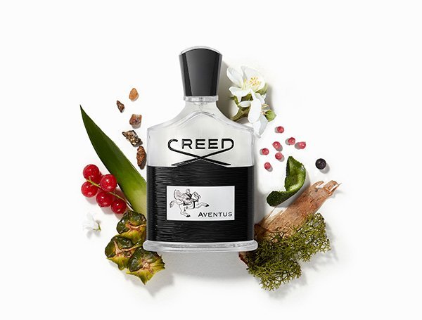 A flat lay shot of The House of Creed's Aventus fragrance bottle sat on a bed of florals and fruits on a white background.
