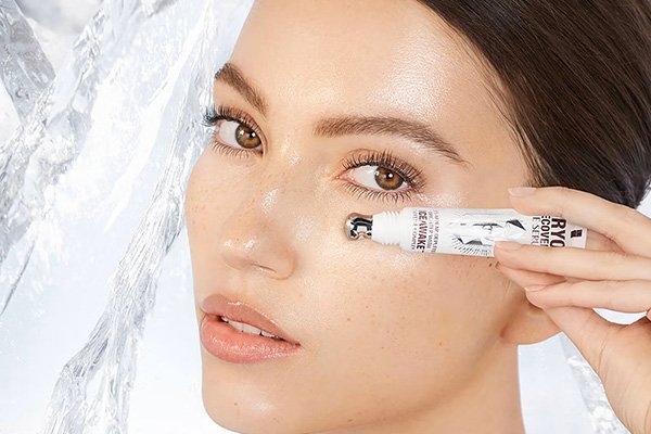 A close-up of a model applying the Charlotte Tilbury Cryo-Recovery Eye Serum under her eyes, with her face next to a block of ice.